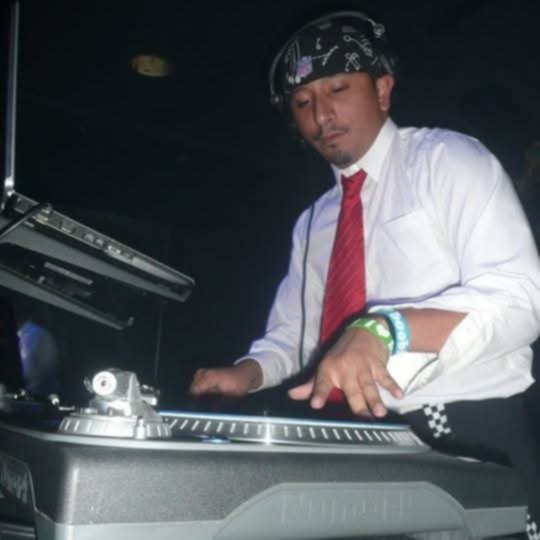 DJ R Styles spinning vinyl in a bandana and tie